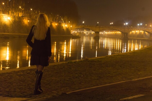 Zdjęcie z tyłu widok kobiety idącej na promenadzie nad rzeką tybru w nocy