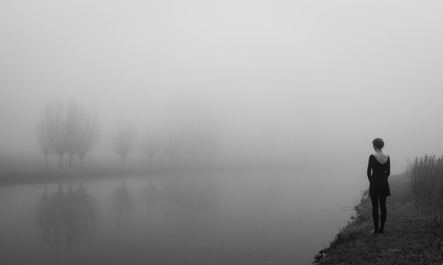 Zdjęcie z tyłu widok kobiety patrzącej na jezioro w mglistą pogodę