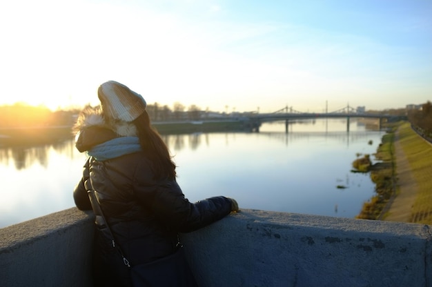 Zdjęcie z tyłu widok kobiety patrzącej na rzekę, stojącej na tle nieba podczas zachodu słońca