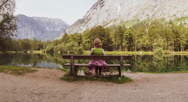 Zdjęcie z tyłu widok kobiety siedzącej na ławce nad jeziorem na tle gór