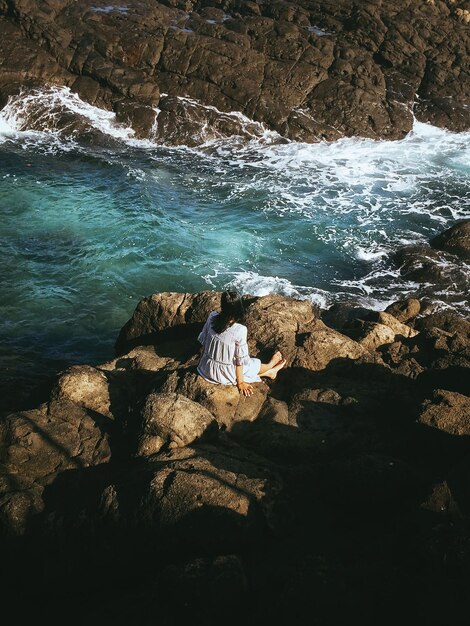 Z tyłu widok kobiety siedzącej na skale nad morzem
