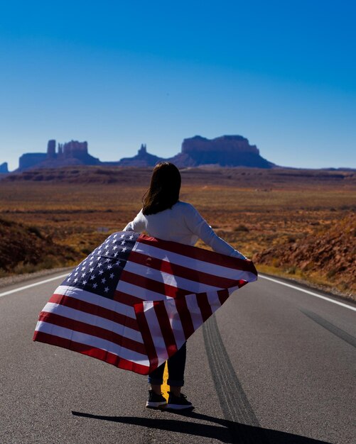 Zdjęcie z tyłu widok kobiety trzymającej flagę stojącej na drodze