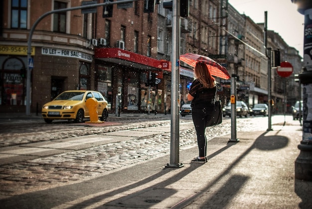 Z tyłu widok kobiety trzymającej parasol, stojącej na chodniku
