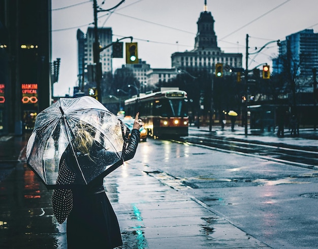 Zdjęcie z tyłu widok kobiety z parasolem stojącej na mokrej ulicy w czasie monsunów