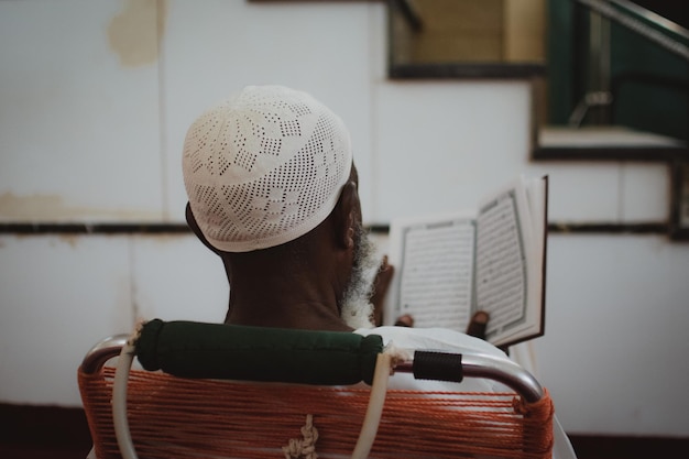 Z tyłu widok mężczyzny z szarą brodą czytającego Koran w meczecie