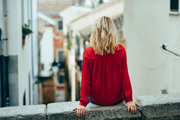 Z tyłu widok młodej kobiety siedzącej na balustradzie w mieście