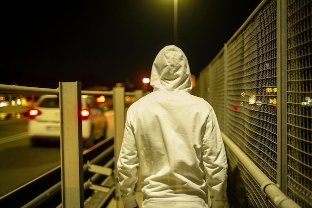 Zdjęcie z tyłu widok osoby z hoodle chodzącej w nocy po drodze z samochodami na ulicy koncepcja ludzi miejskiego stylu życia bezpieczeństwo i przestępczość spacer po moście
