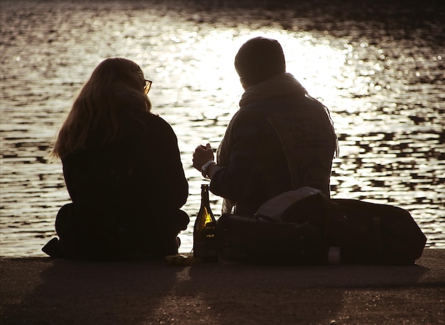 Z tyłu widok pary siedzącej na plaży podczas zachodu słońca