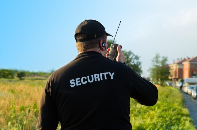 Zdjęcie z tyłu widok strażnika rozmawiającego przez walkie-talkie na polu