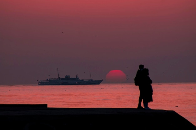 Zdjęcie z tyłu widok sylwetki kobiety stojącej na plaży na tle nieba podczas zachodu słońca