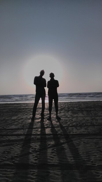 Zdjęcie z tyłu widok sylwetkowych przyjaciół stojących na brzegu podczas zachodu słońca