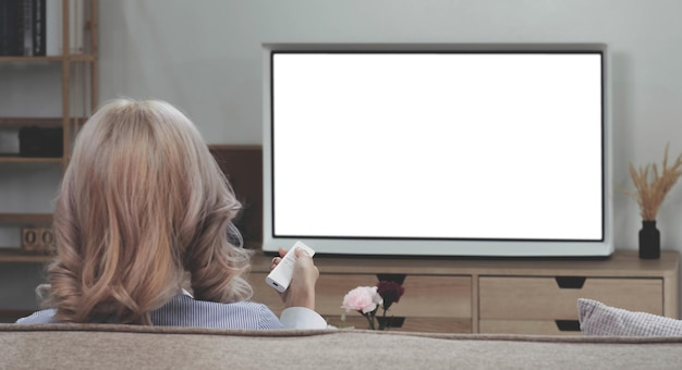 Za azjatycką młodą kobietą oglądającą biały ekran telewizora na kanapie w domu