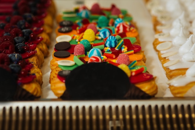 Za Słodkie. Pyszne świeże Eklery Ozdobione Kolorowymi Słodyczami Ustawionymi Blisko Siebie Na Wystawie