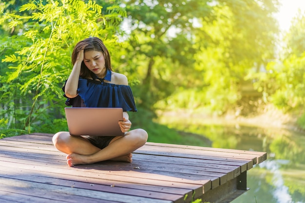 Zaakcentowana kobieta używa laptop na drewnianym jetty