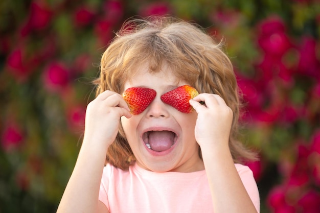 Zabawa dla dzieci z truskawkami szczęśliwe zabawne dziecko trzymające truskawki latem na świeżym powietrzu