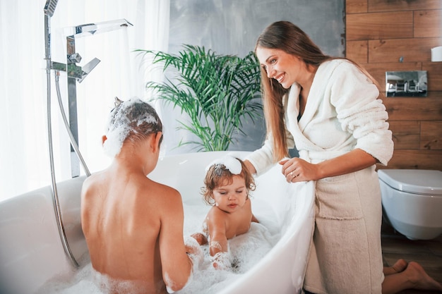 Zabawa Młoda mama pomaga synowi i córce Dwoje dzieci myje się w wannie