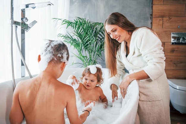 Zabawa Młoda mama pomaga synowi i córce Dwoje dzieci myje się w wannie