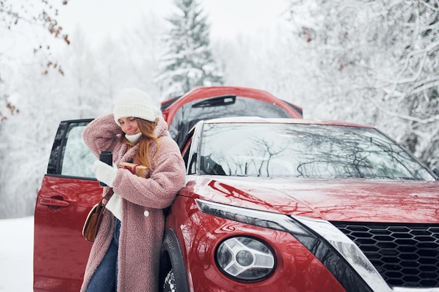 Zabawa Piękna młoda kobieta jest na zewnątrz w pobliżu swojego czerwonego samochodu w okresie zimowym