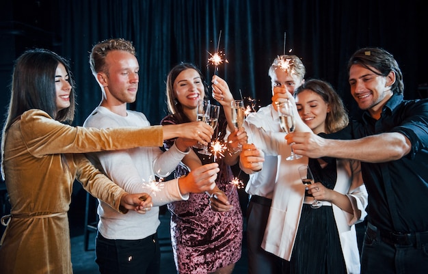 Zabawa z ognie. Grupa wesołych przyjaciół z okazji Nowego Roku w pomieszczeniu z napojami w rękach.