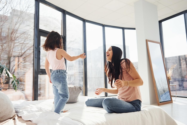 Zabawa z poduszką na łóżku Młoda mama z córką spędzają razem weekend w pokoju