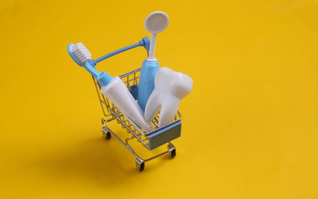 Zabawka sprzęt dentysty w wózku na zakupy na żółtym tle.