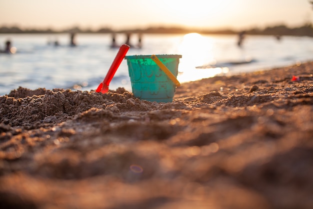 Zabawki dla dzieci do zabawy na piasku. Plastikowe wiadro i grabie na plaży o zachodzie słońca. Pojęcie lata, wakacji rodzinnych i wakacji.