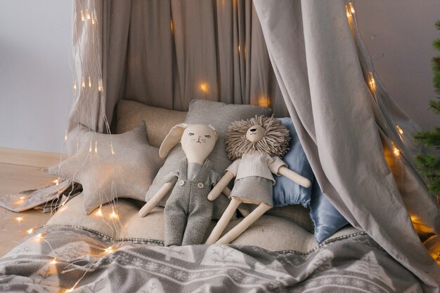 Zdjęcie zabawki na łóżku otoczone poduszkami na łóżeczku otoczonym świątecznymi lampkami