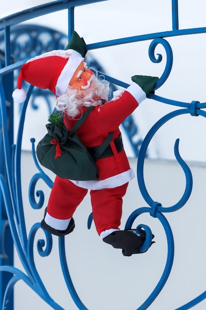Zabawkowy Mikołaj wspina się z torbą prezentów na balkonie chaty wzdłuż balustrady