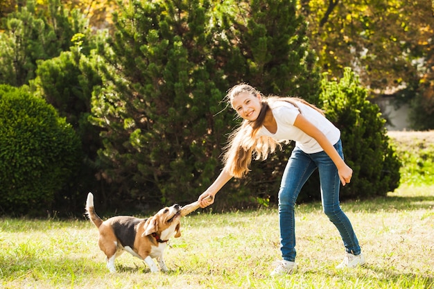 Zabawna dziewczyna rzucająca kijem dla aktywnego psa rasy beagle w parku