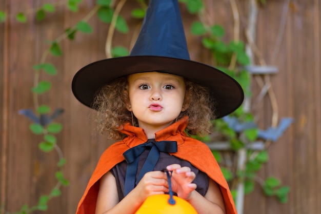 Zabawna dziewczyna w pomarańczowym stroju czarownicy, czarny kapelusz, Boo. Dziecko Halloween. straszne jesienne wakacje