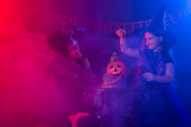 Zabawna dziewczynka i kobieta w strojach czarownic na Halloween z dyniowym Jackiem i psem