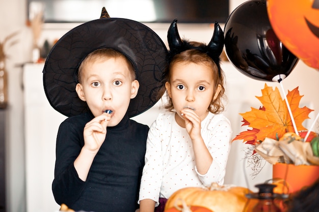 Zabawna dziewczynka i nastolatek w strojach czarownicy i zła na imprezę Halloween jedzące cukierki na patyku i baw się dobrze