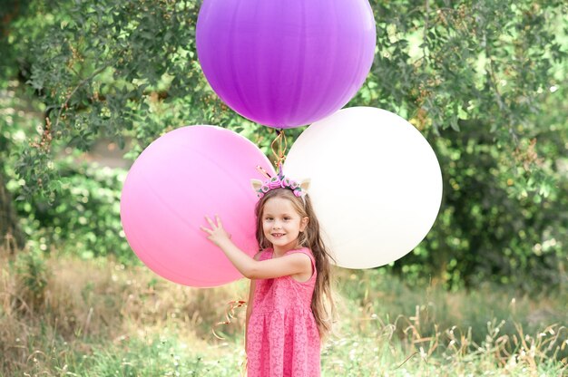 Zabawna dziewczynka trzymająca kolorowe balony w parku