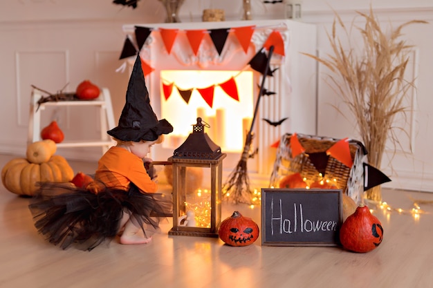 Zdjęcie zabawna dziewczynka w stroju czarownicy halloween z dyniowym gniazdem i miotłą w pomieszczeniu
