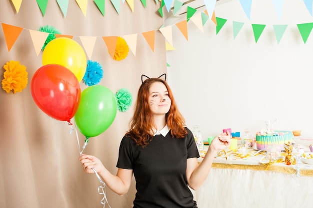 Zabawna figlarna animatorka w kostiumie kota trzymającego kolorowe kulki na przyjęciu urodzinowym