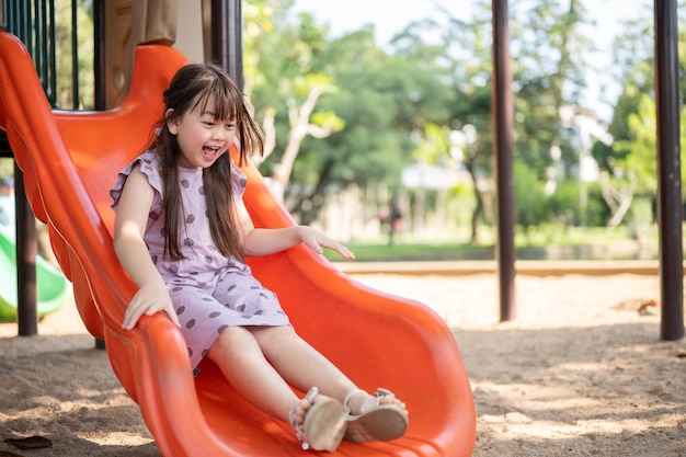 Zabawna i wesoła młoda azjatycka dziewczyna gra w kolorową slajdę na placu zabaw w parku
