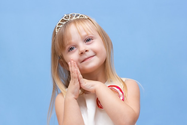 Zabawna mała księżniczka dziewczynka w srebrnej koronie i różowej sukience na niebieskim tle