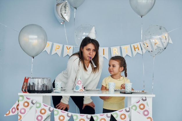 Zabawna młoda kobieta bawi się przygotowując urodzinowy stół z małą dziewczynką