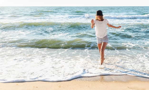 Zabawna młoda kobieta figlarny na plaży o zachodzie słońca. Piękna szczęśliwa kobieta na brzegu błękitnego morza, bawiąc się, pozytywny nastrój, wakacje, słoneczna koncepcja