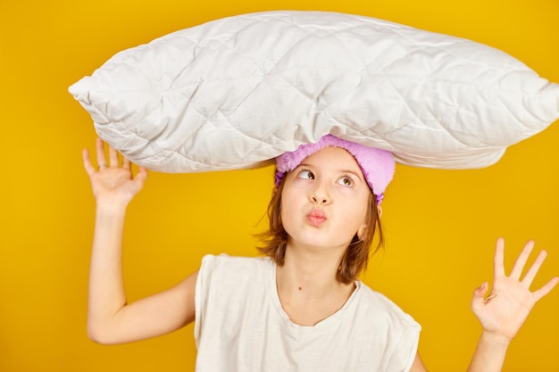 Zabawna nastolatka w białej piżamie z fioletową maską do spania trzyma poduszkę