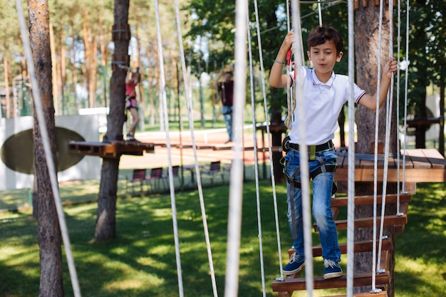 Zabawna rozrywka. Wesoły chłopiec preteen bawi się w parku linowym podczas spaceru po szlakach