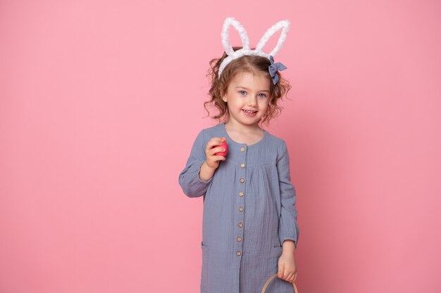 Zabawne dziecko dziewczynka w uszy Zajączka wielkanocnego trzymając kosz z kolorowymi jajkami.