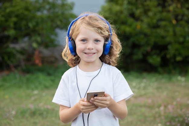 Zabawne dziecko z długimi włosami słuchające muzyki z niebieskimi telefonami i telefonem komórkowym