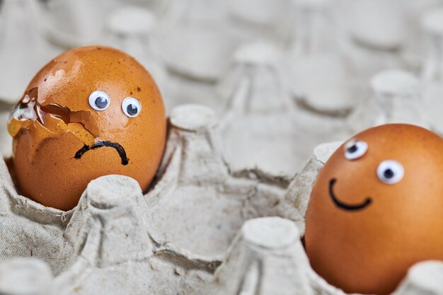 Zdjęcie zabawne jajko i smutne pęknięte jajko w papierowej tacce na jajka dwa świeże i naturalne jajka kurczaka wielkanocne
