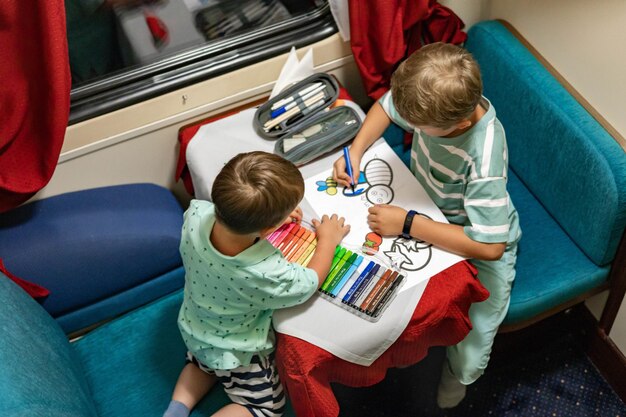 Zabawni mali bracia podróżują pociągiem jadąc wygodnym wagonem kolejowym, rysując obraz