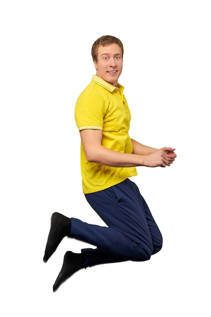 Zabawny atrakcyjny facet w żółtej koszulce i niebieskich spodniach skaczących na białym tle