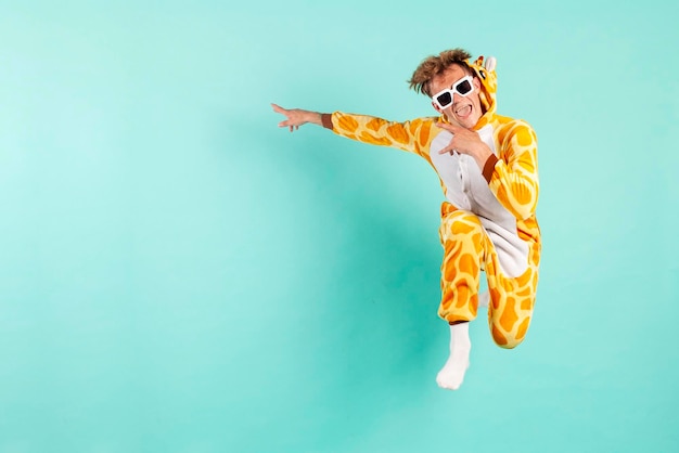 Zabawny facet zwycięzca w pomarańczowej piżamie żyrafy skacze i wskazuje na bok na imprezie w okularach przeciwsłonecznych