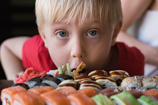 Zabawny jasnowłosy chłopiec gapi się na sushi Chłopiec w kawiarni Koncepcja kuchni azjatyckiej