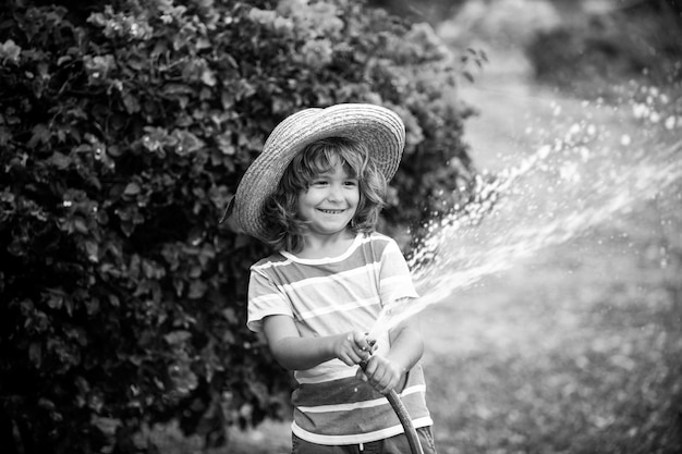 Zabawny mały chłopiec bawi się wężem ogrodowym na podwórku. Dziecko bawi się sprayem wody. Letnia aktywność na świeżym powietrzu dla dzieci.