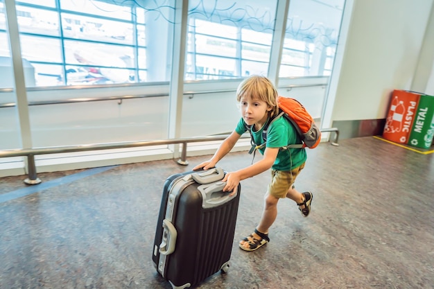 Zabawny mały chłopiec jedzie na wakacje z walizką na lotnisku w pomieszczeniu